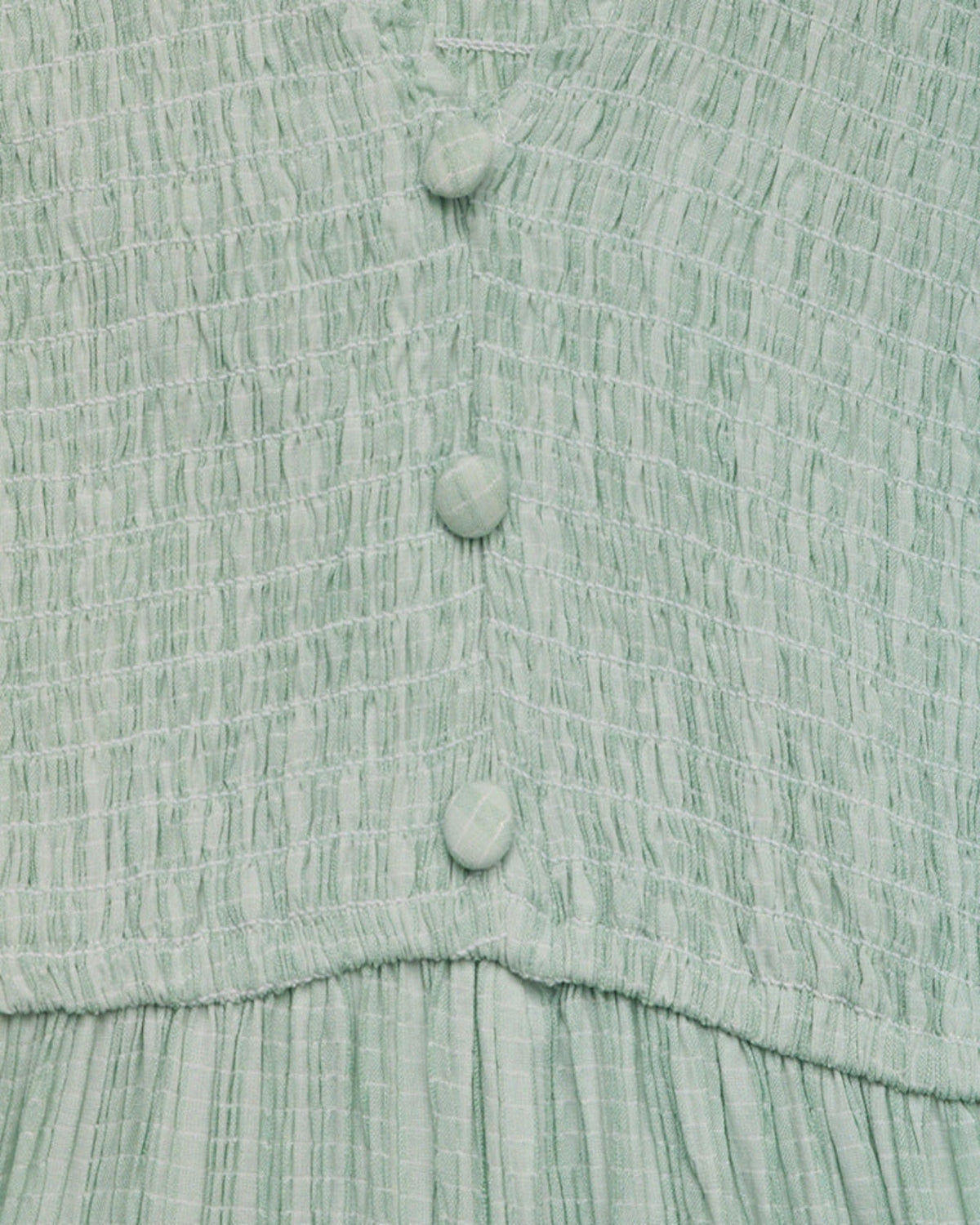 Close-up of a textured green dress with buttons on a matching fabric background
