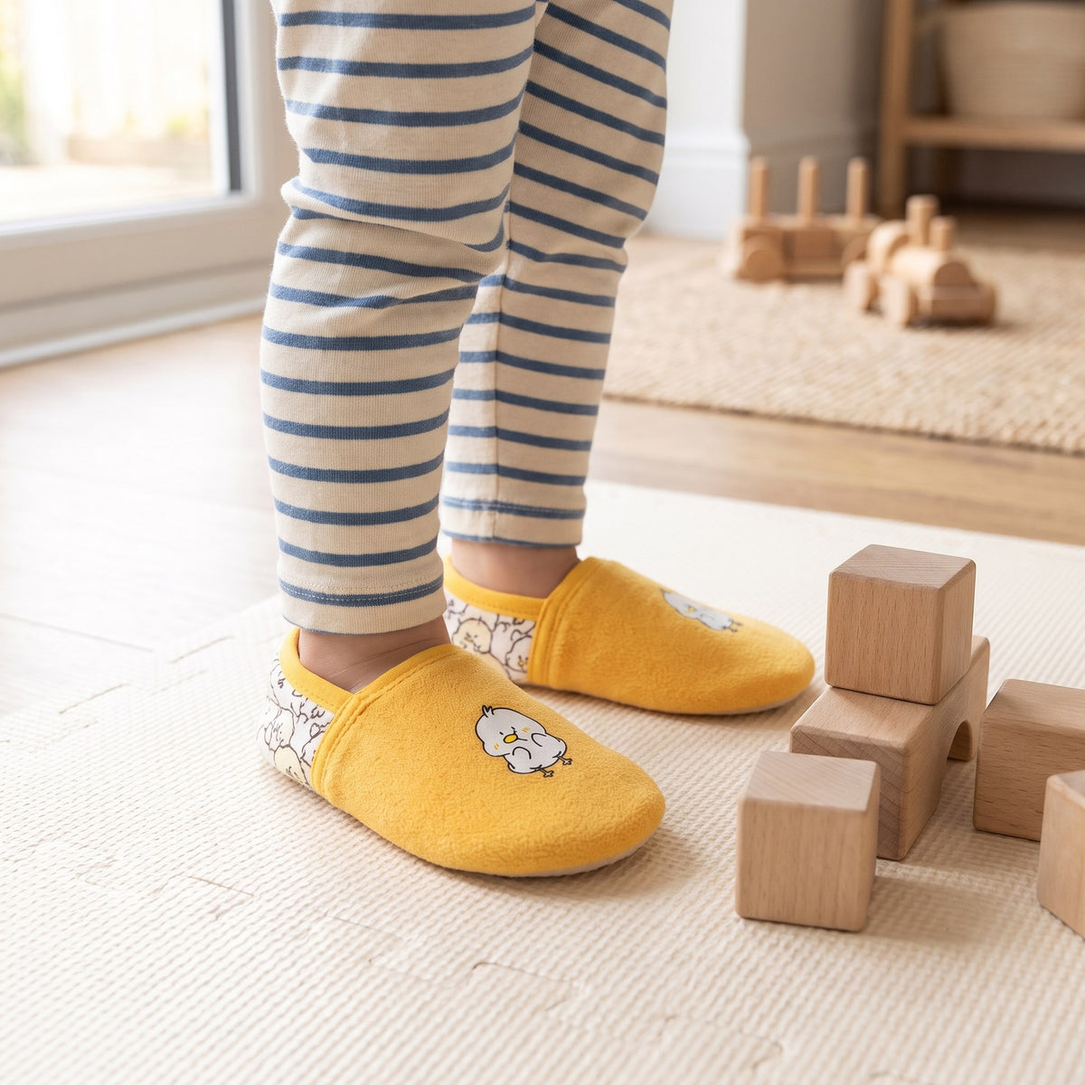 Toddler wearing yellow duck slippers on a play mat with building blocks