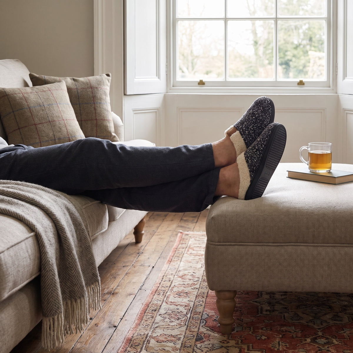 Man relaxing with feet on a footstool wearing grey memory foam slippers