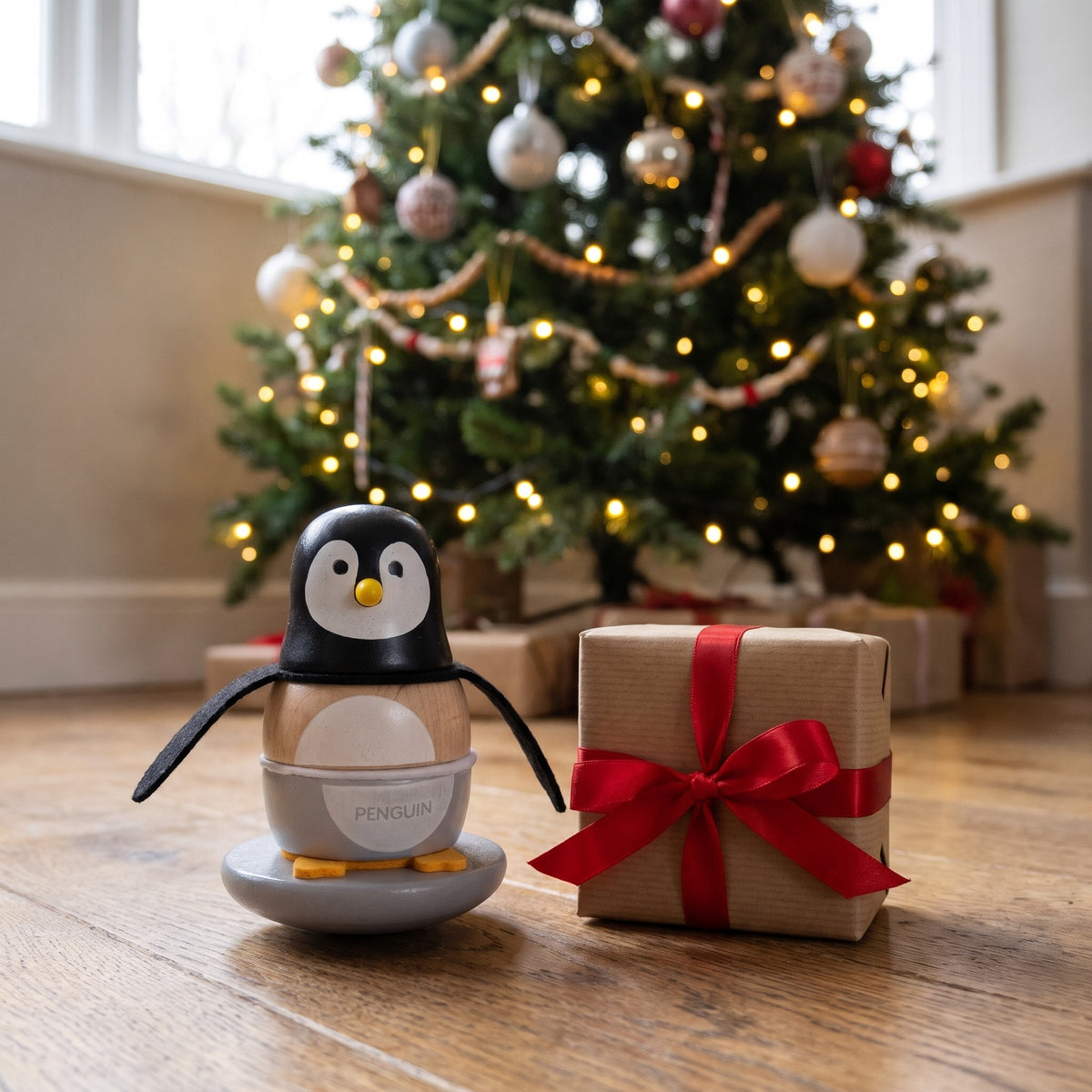 Wooden penguin stacker in front of a Christmas tree with a small present