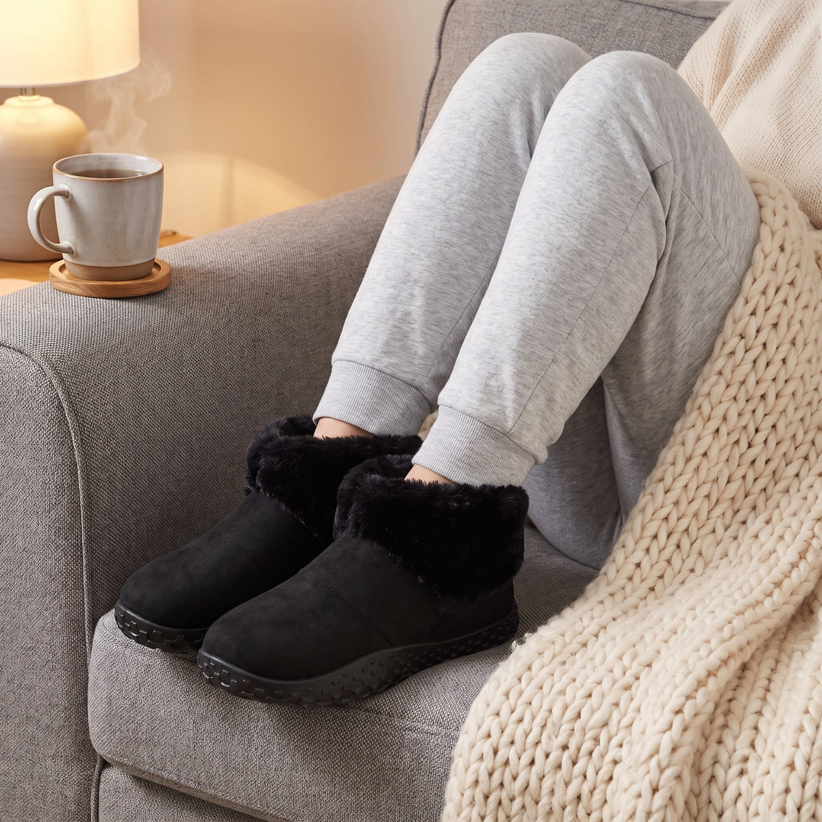 Woman relaxing on a sofa wearing black faux fur slipper boots