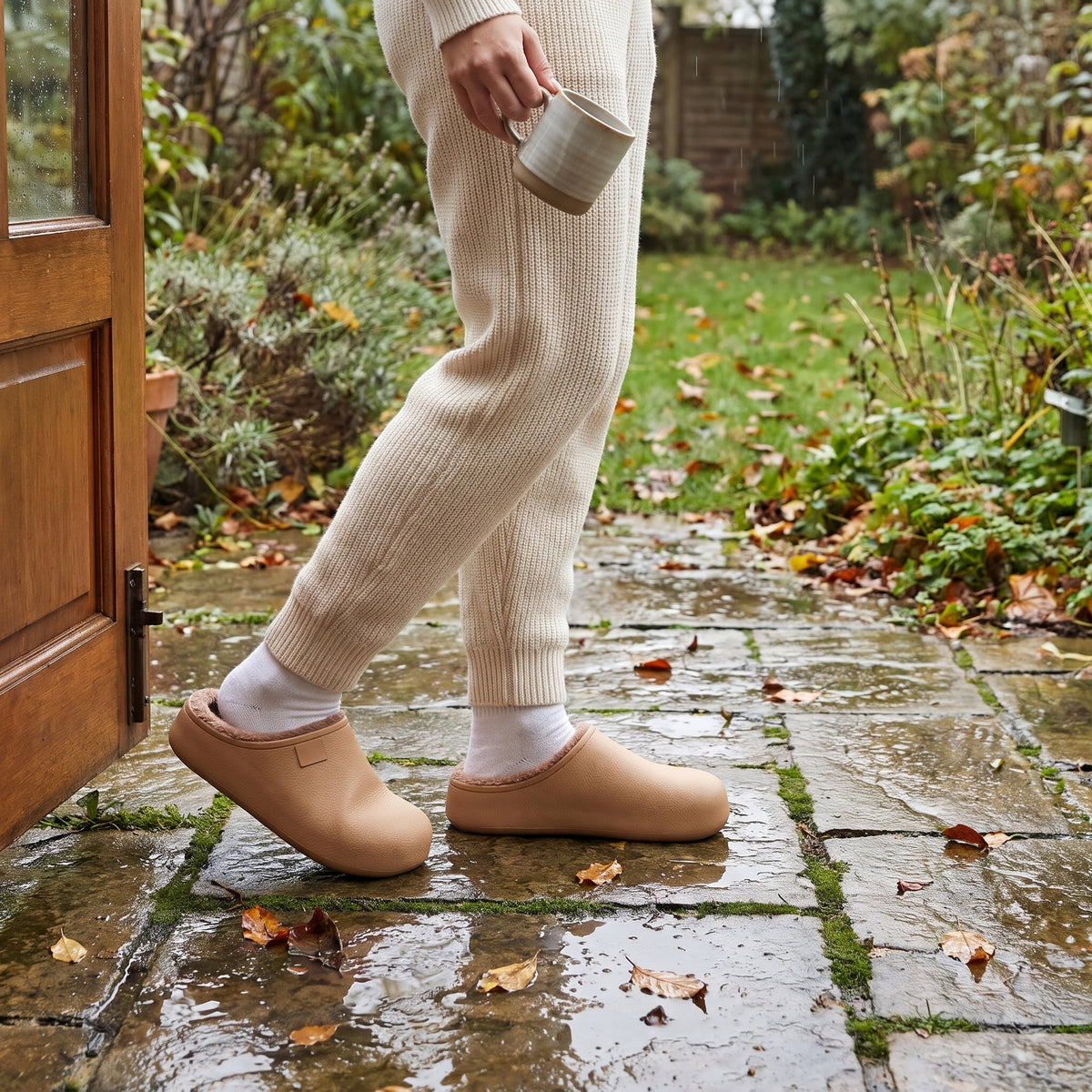 Woman stepping onto a wet garden patio in tan waterproof clog slippers