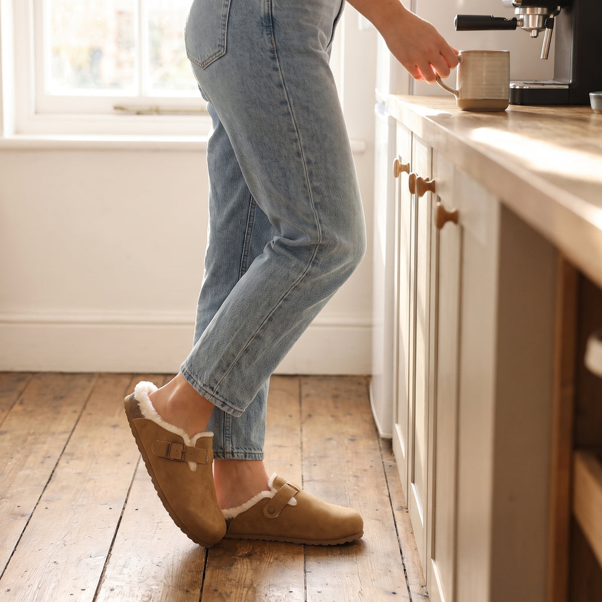 Woman in jeans wearing camel clog slippers in a kitchen