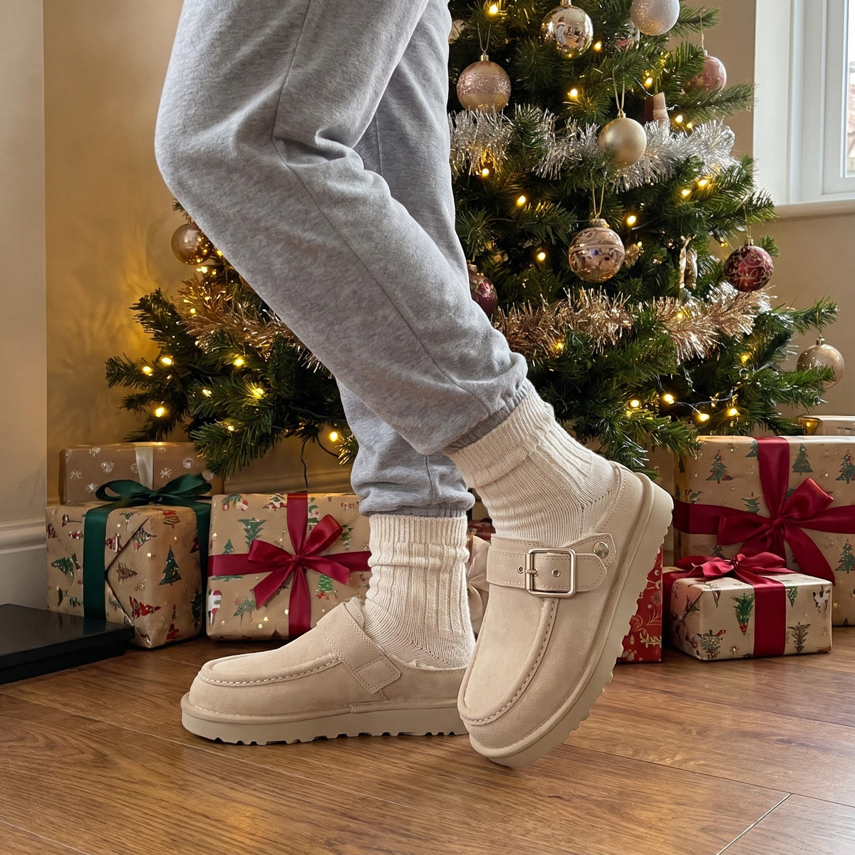 Sand suede clog slippers with cream socks beside a Christmas tree and presents