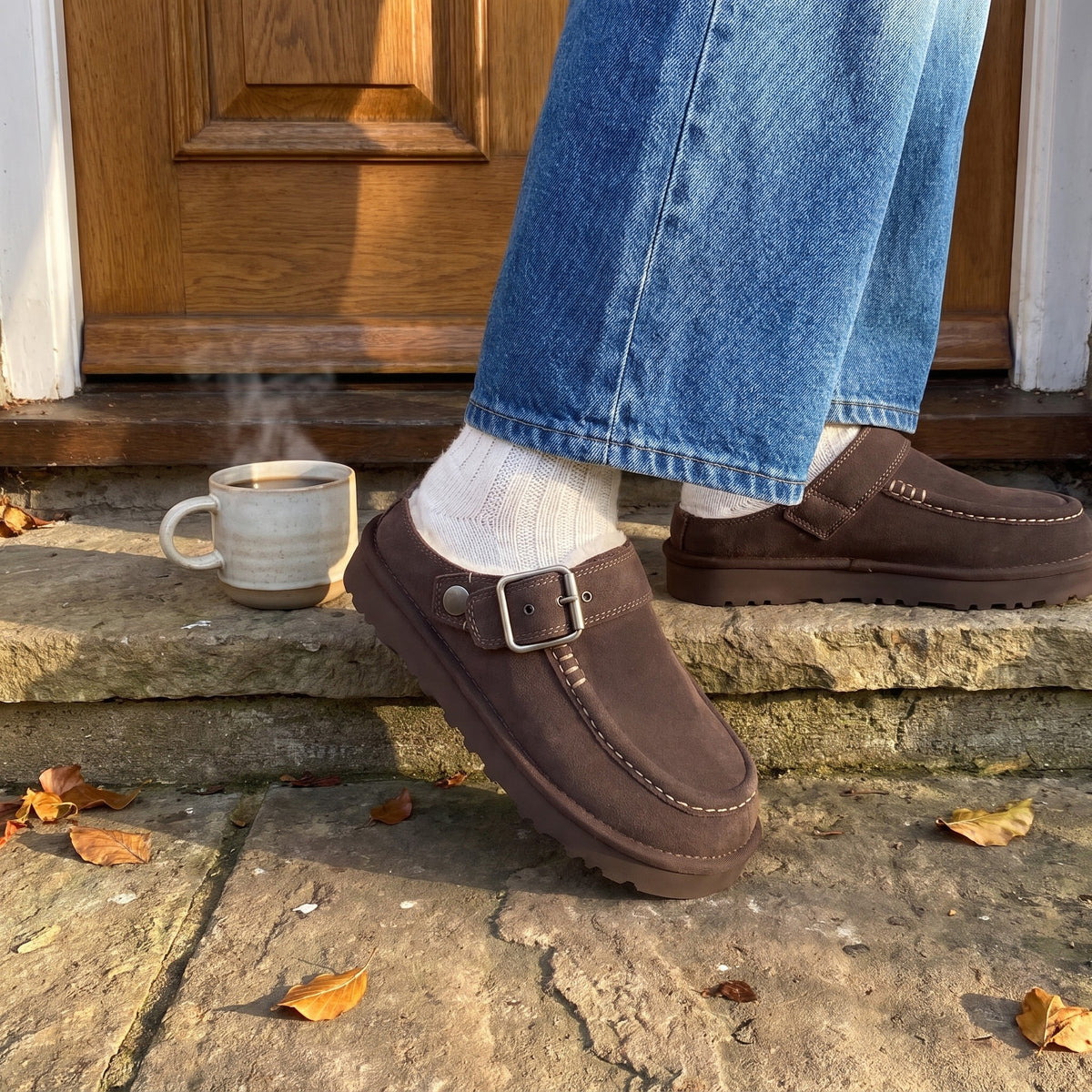 Woman in jeans stepping onto a stone doorstep in brown suede clog slippers