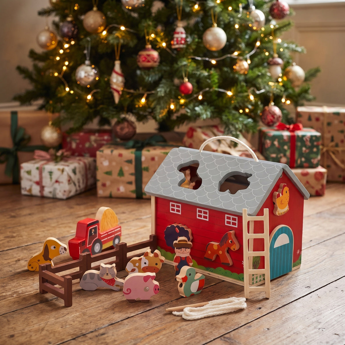 Wooden farm barn toy set with animals under a Christmas tree beside wrapped presents
