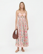 Woman wearing a floral dress holding a brown bag on a white background