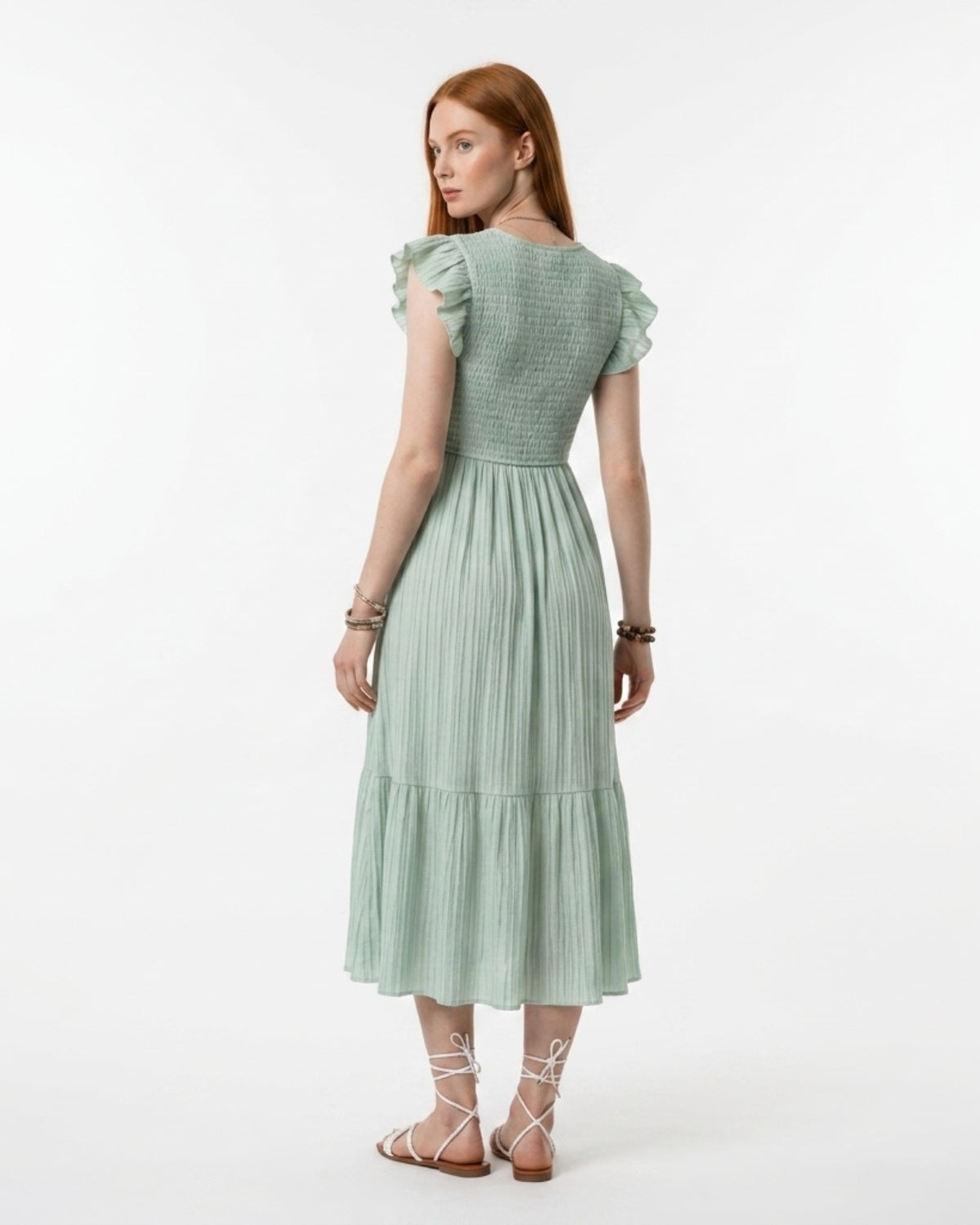 Woman wearing a light green dress with ruffled sleeves on a white background