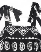 Black dress with white floral patterns and bow details on a white background