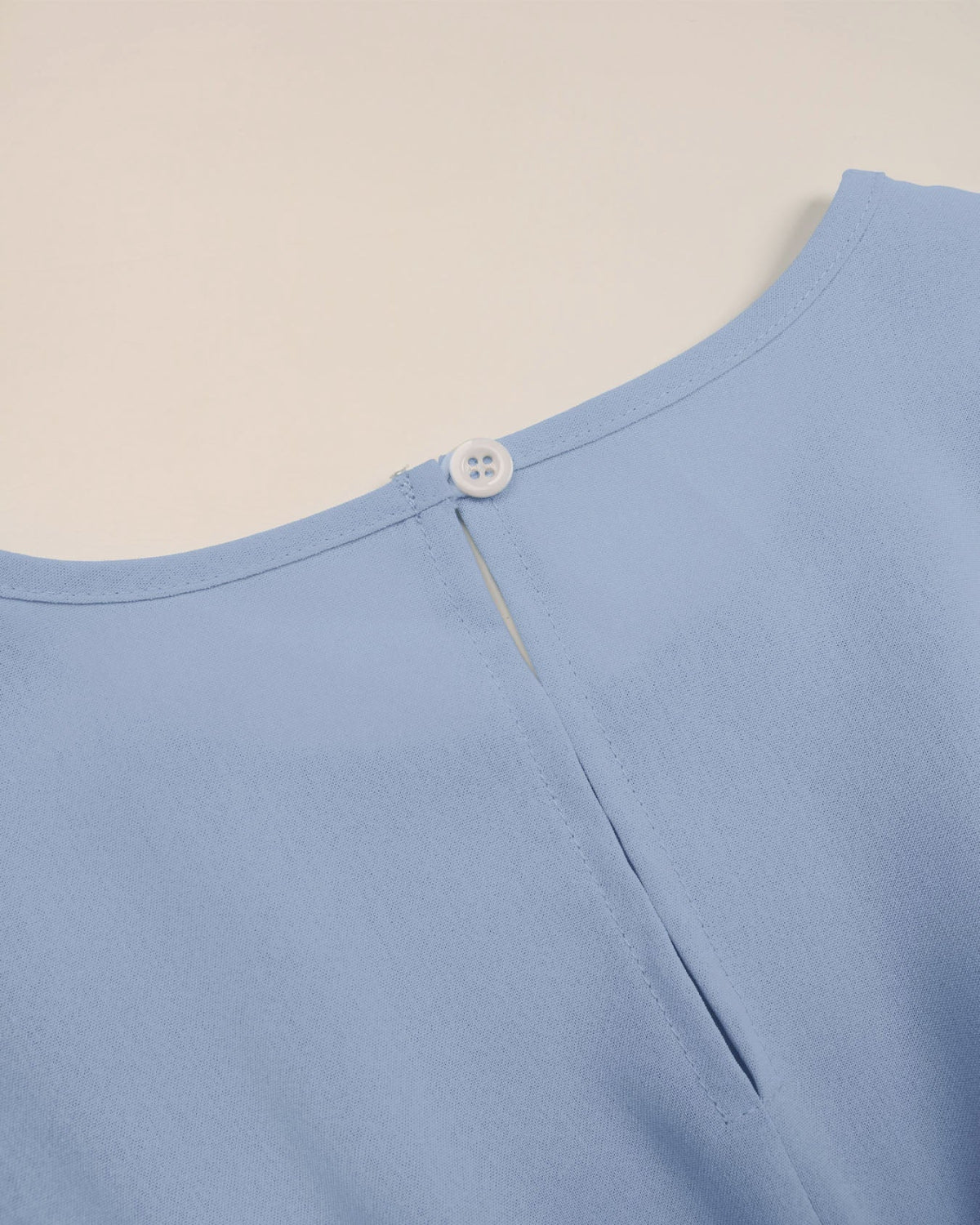 Close-up of a light blue garment with a button on a beige background