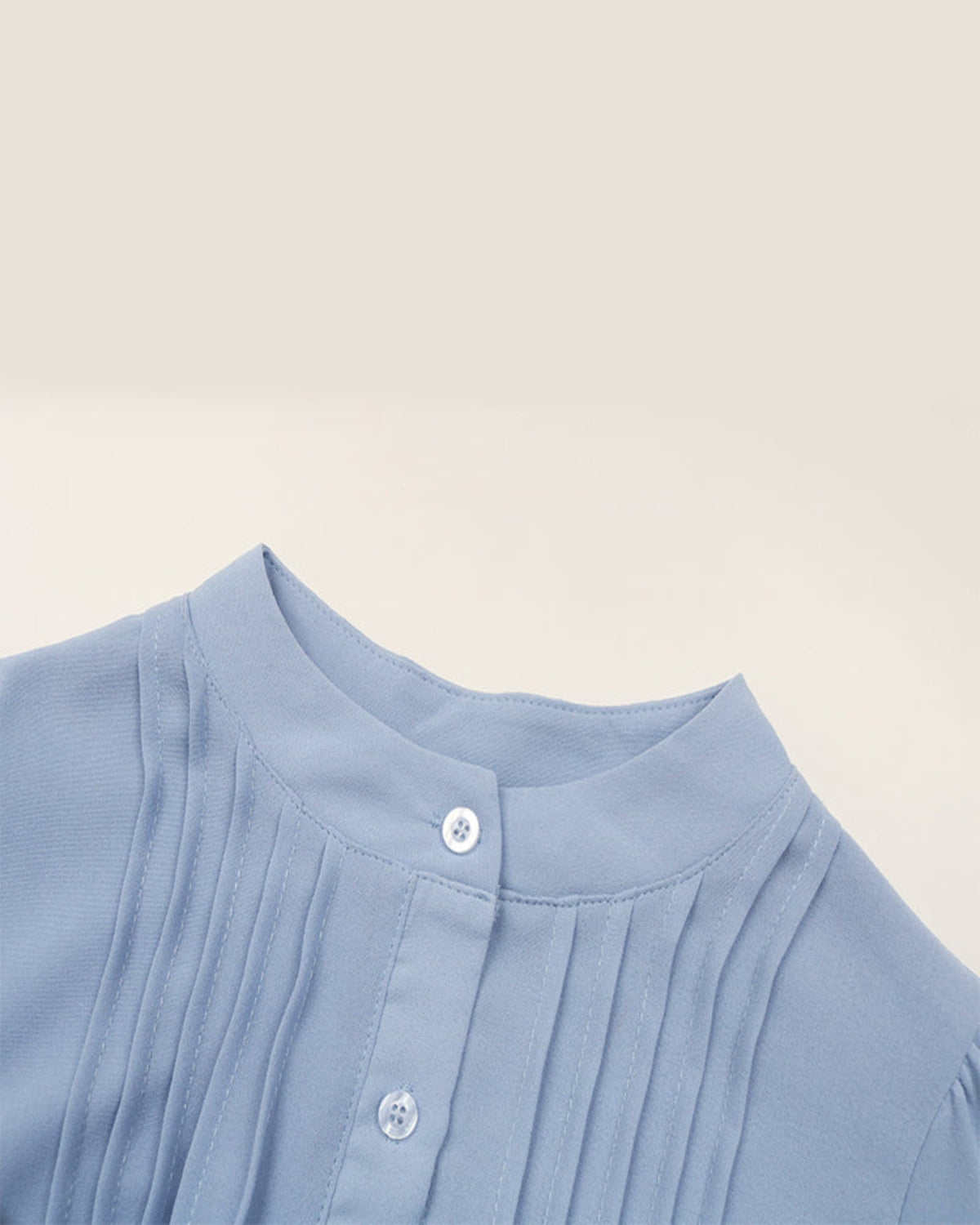 Close-up of a light blue garment with pleated details on a beige background