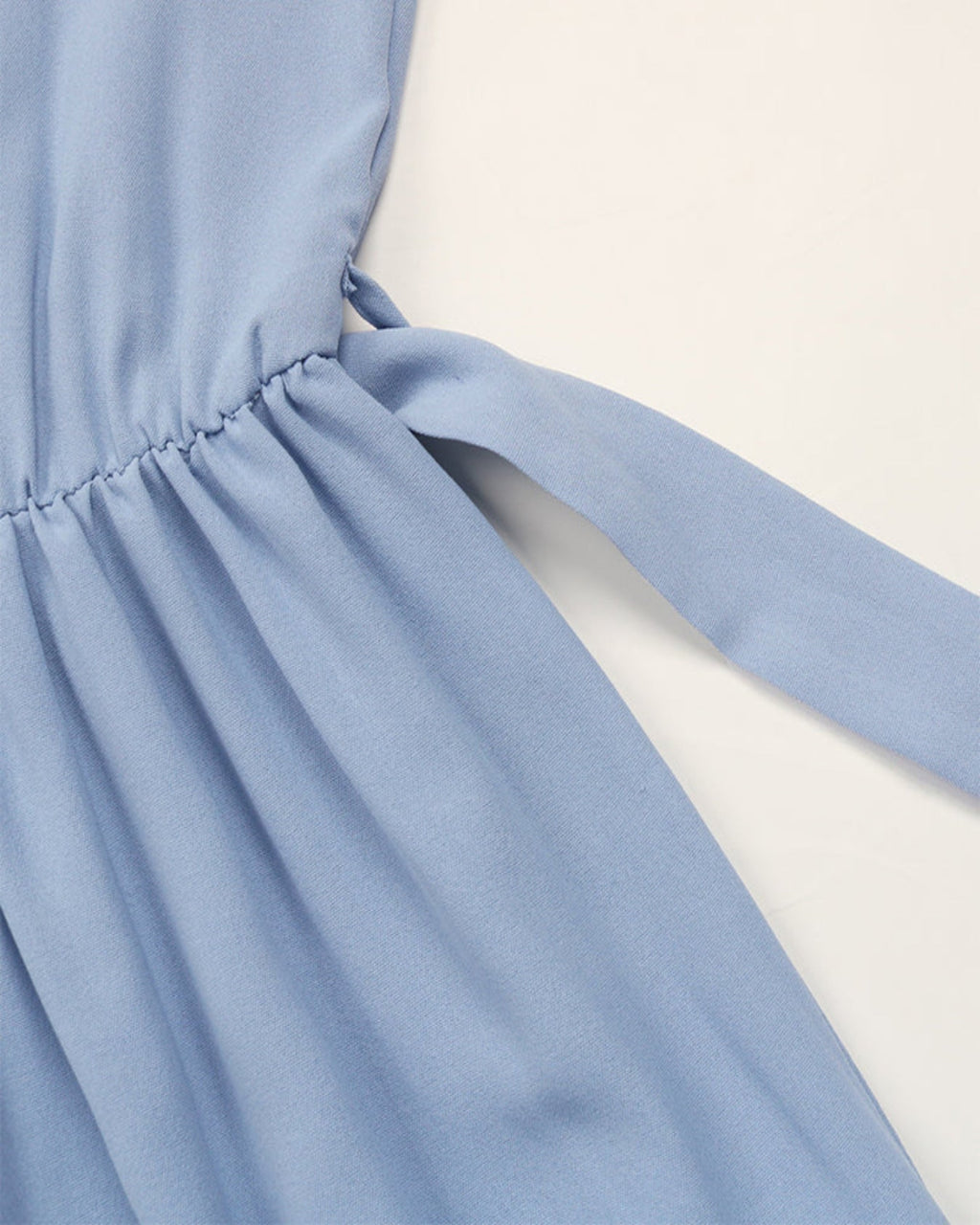 Close-up of a light blue dress with a tie detail on a white background