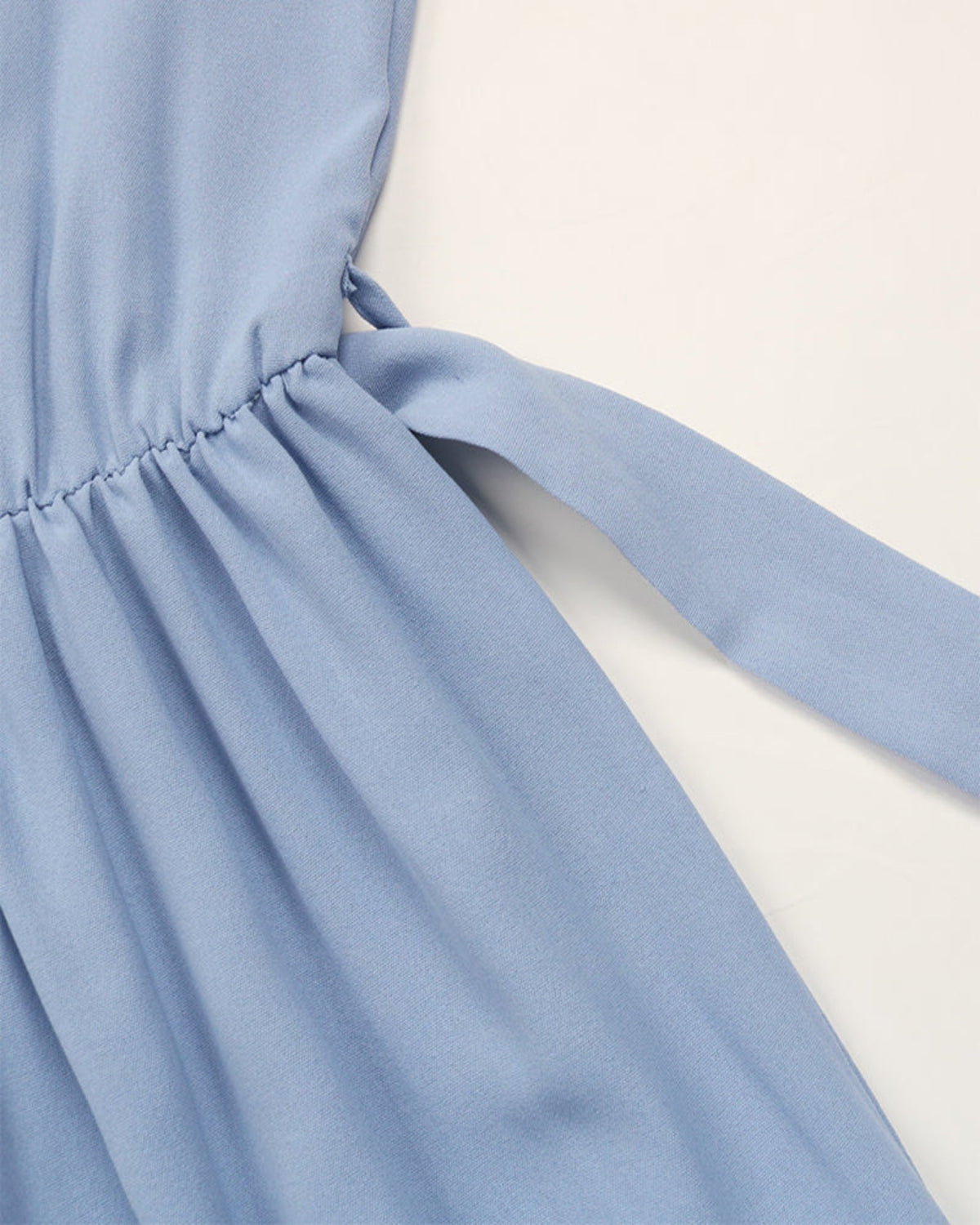 Close-up of a light blue dress with a tie detail on a white background
