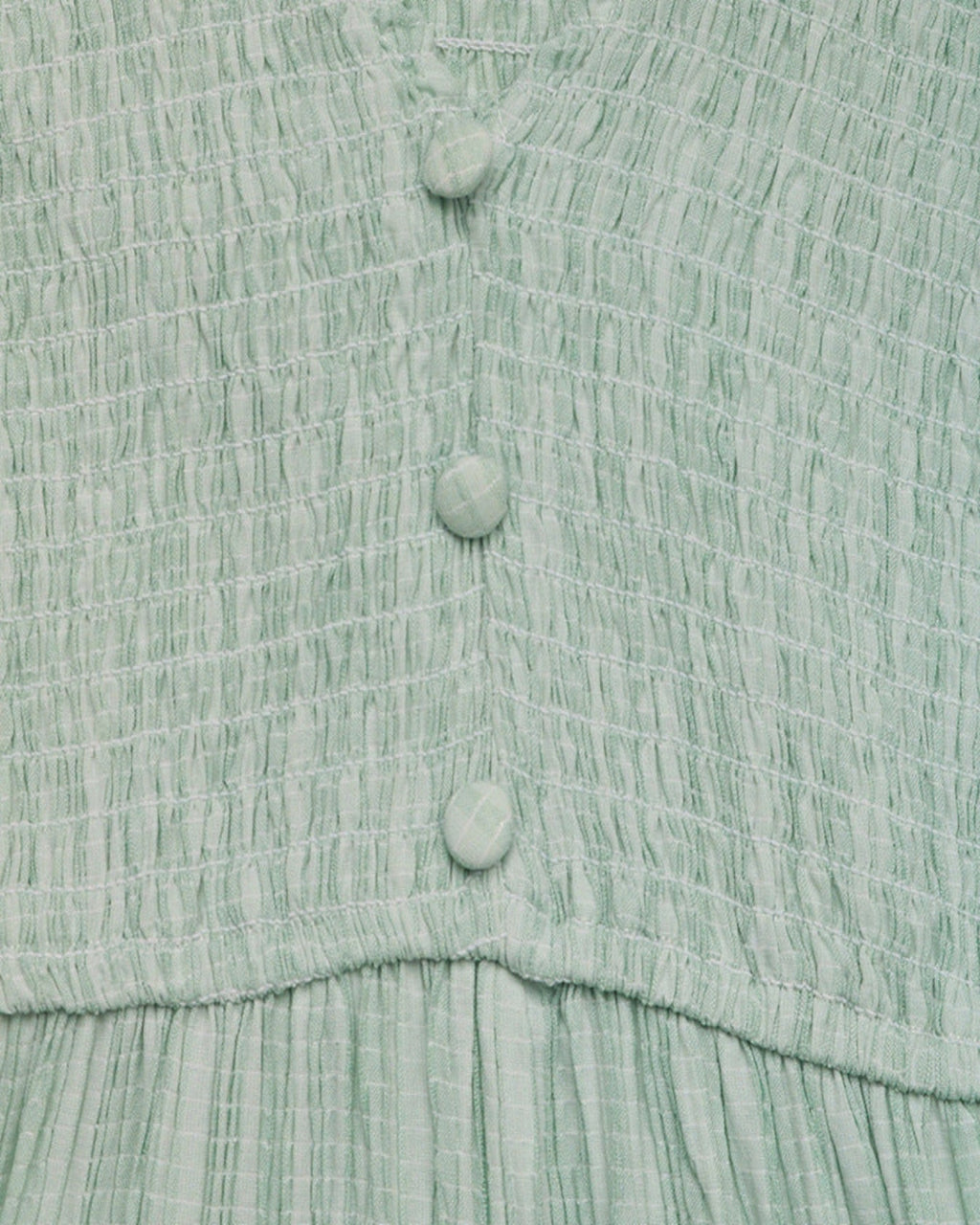 Close-up of a textured green dress with buttons on a matching fabric background