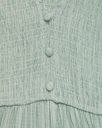 Close-up of a textured green dress with buttons on a matching fabric background