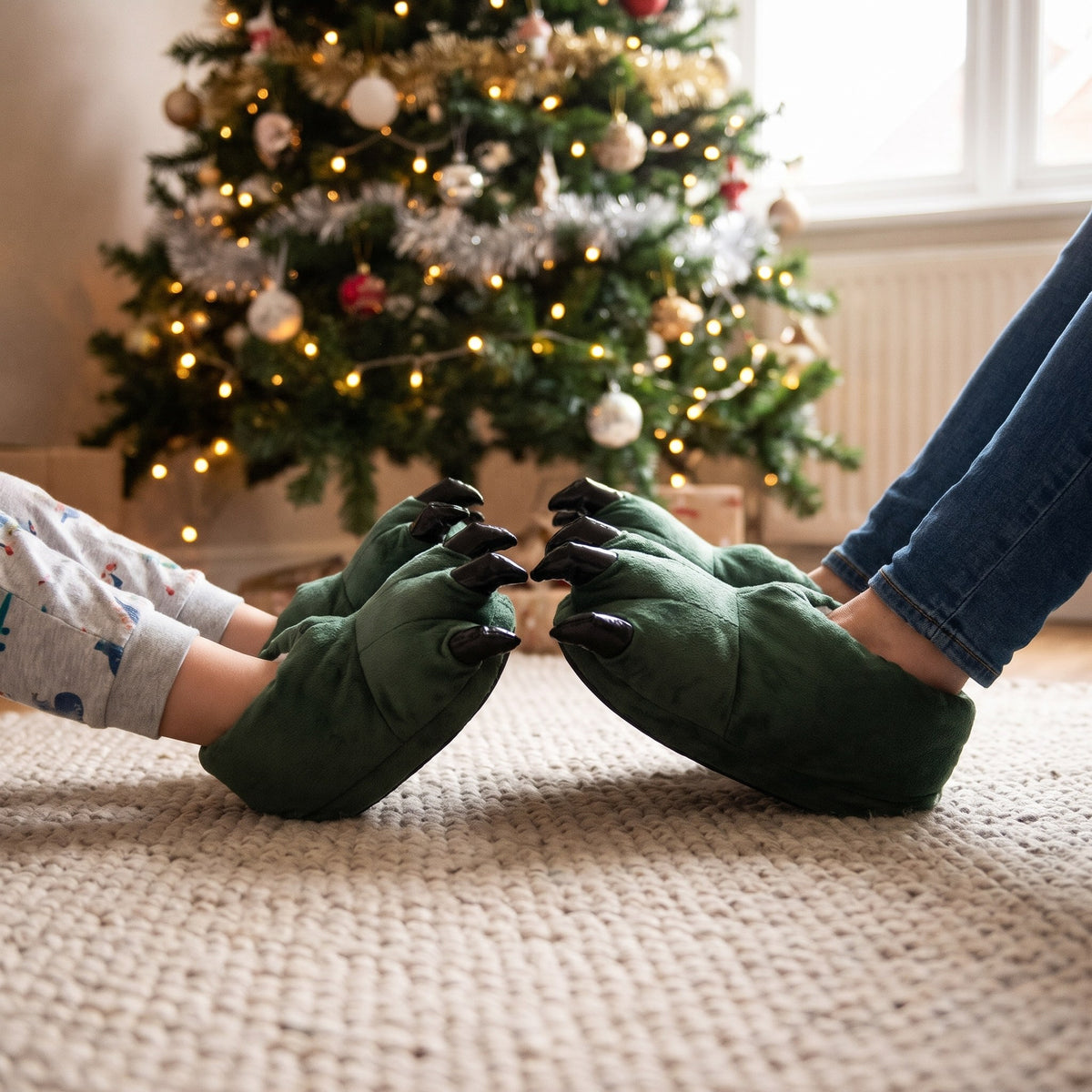 Parent and child wearing matching green dinosaur claw slippers by a Christmas tree