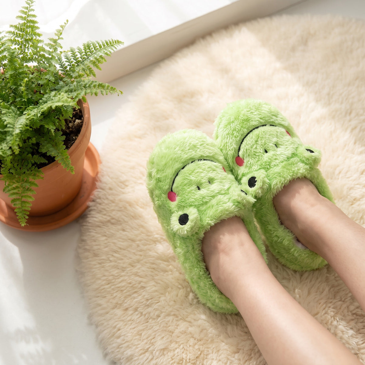 Feet in green frog slippers on a cream rug beside a plant