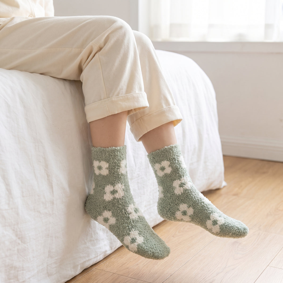Woman sitting on a bed wearing sage daisy fluffy socks