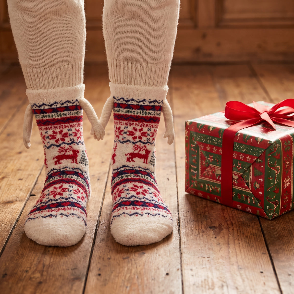 Cream fair isle hand holding socks next to a Christmas present
