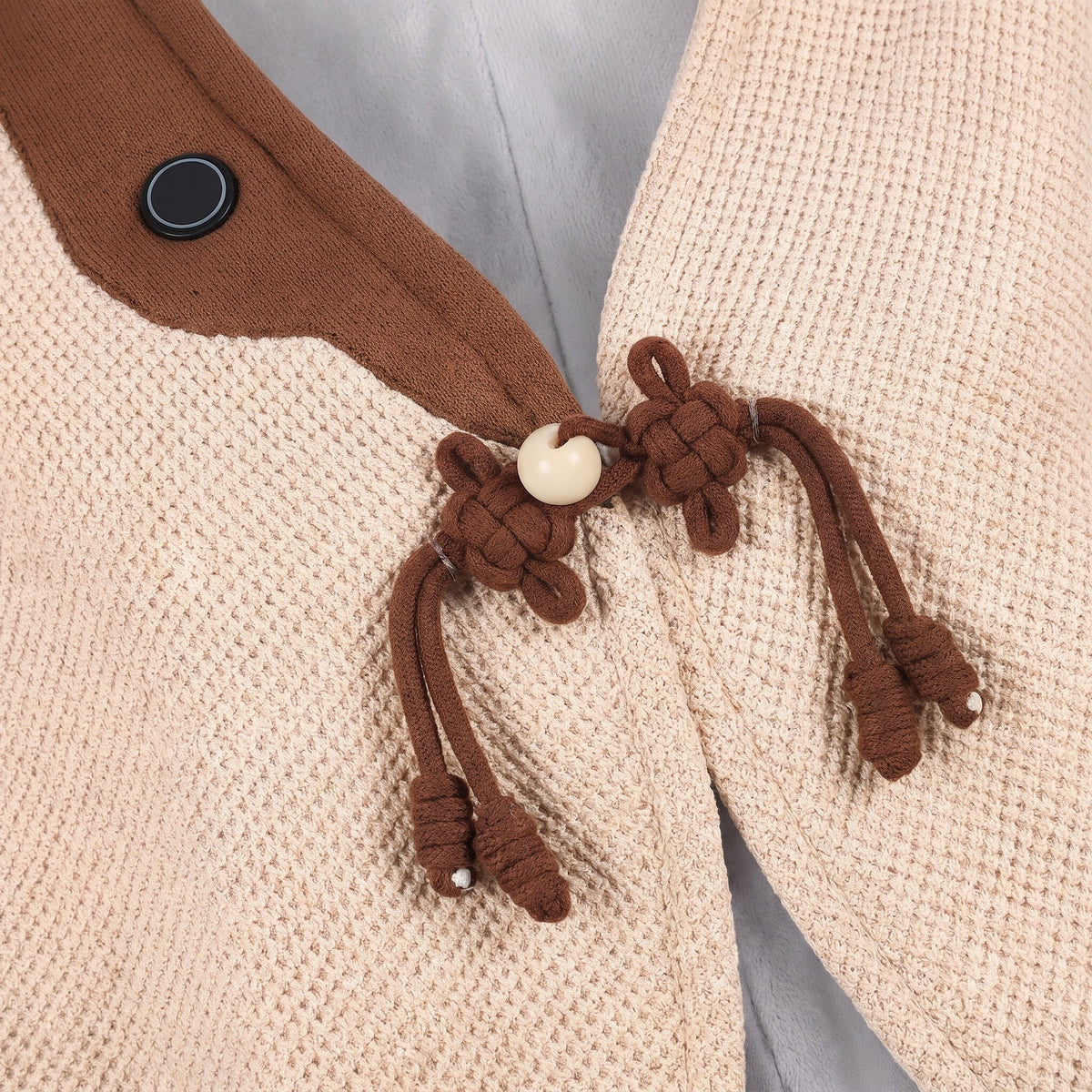 Close up of the brown frog knot closure and heat button on a cream knit cape