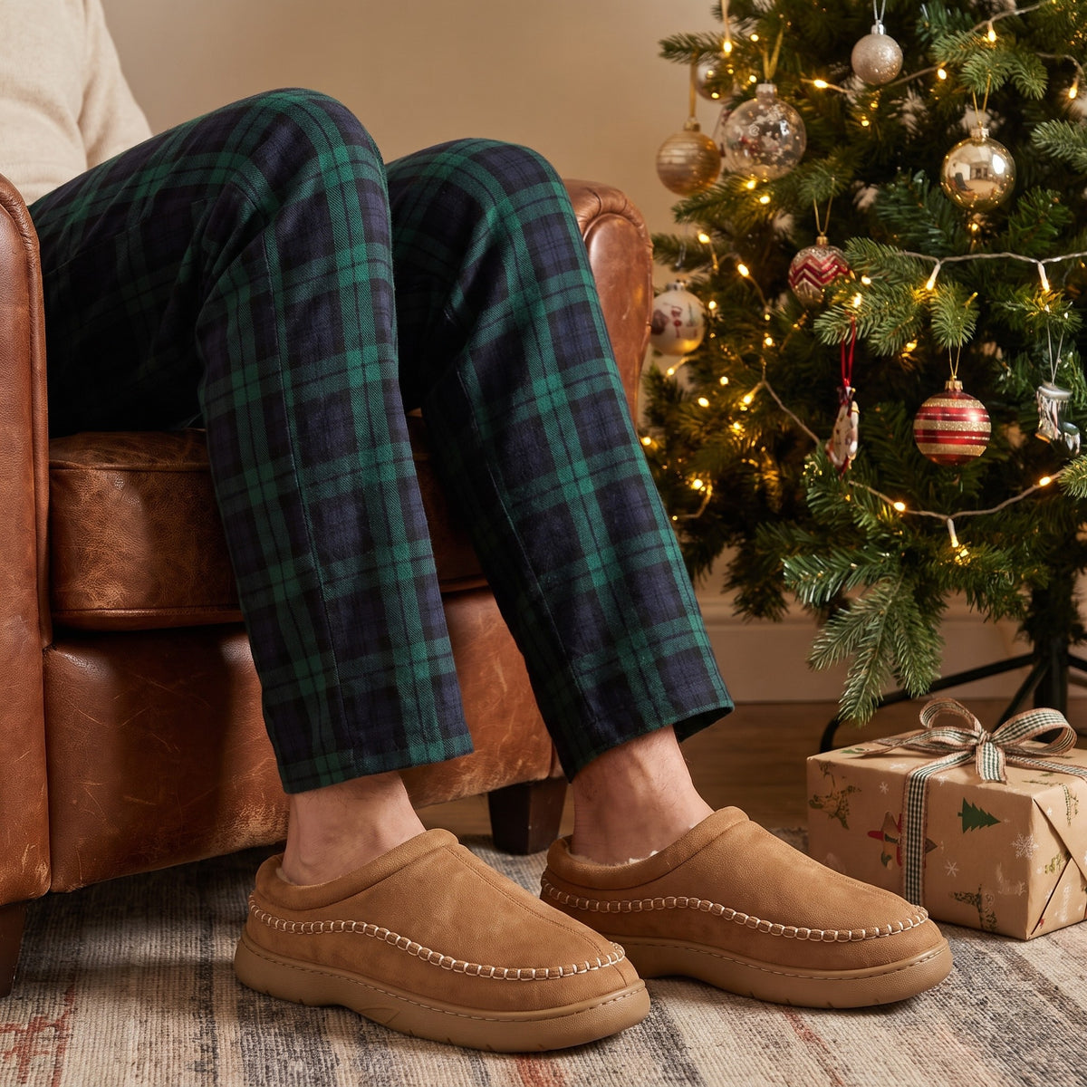 Man in tartan pyjamas and brown clog slippers by a Christmas tree