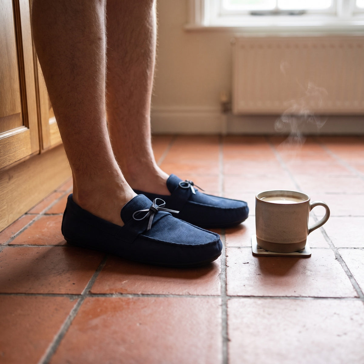 Man in navy moccasin slippers on terracotta kitchen tiles with a coffee