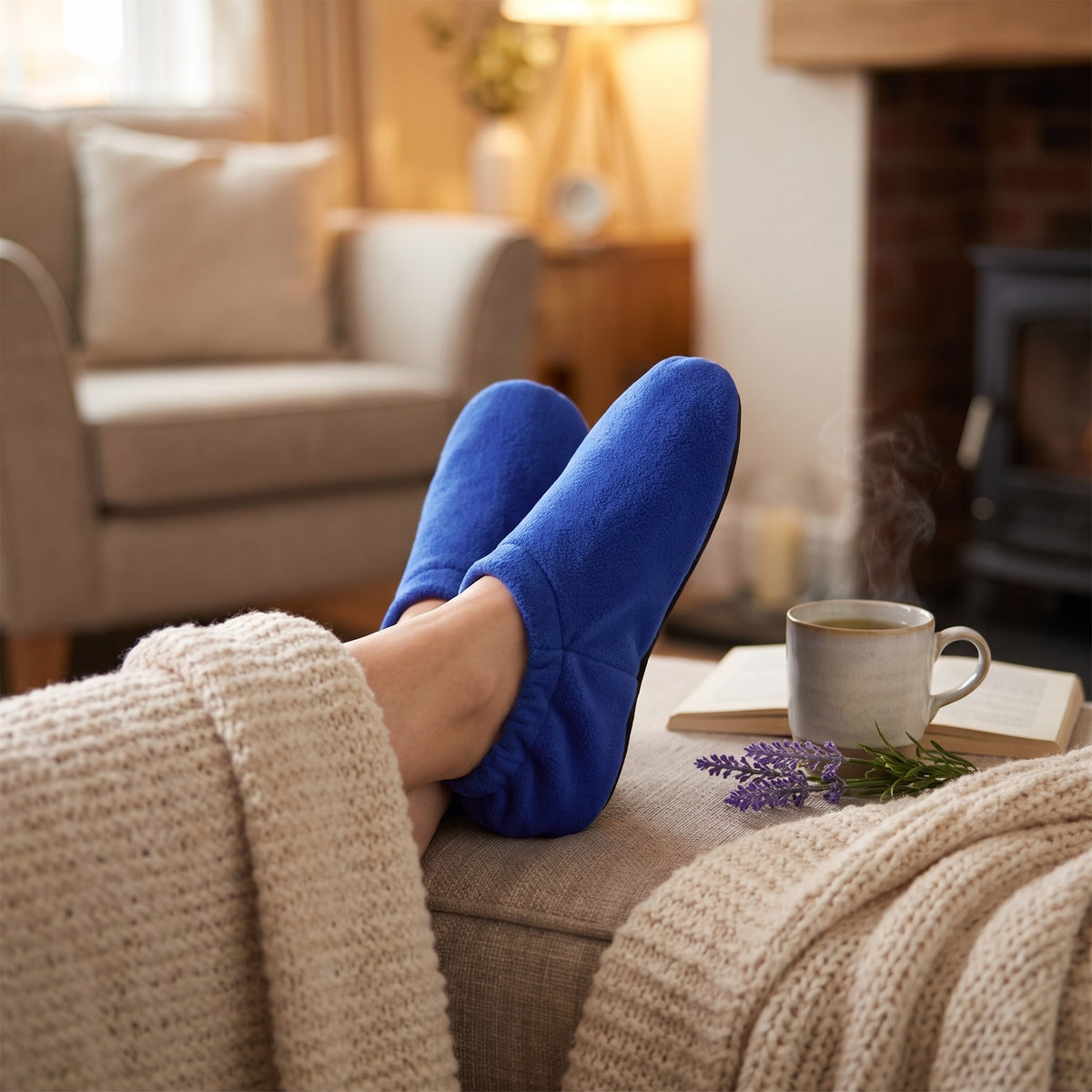 Feet resting on a footstool in blue microwavable heated slippers with herbal tea and lavender