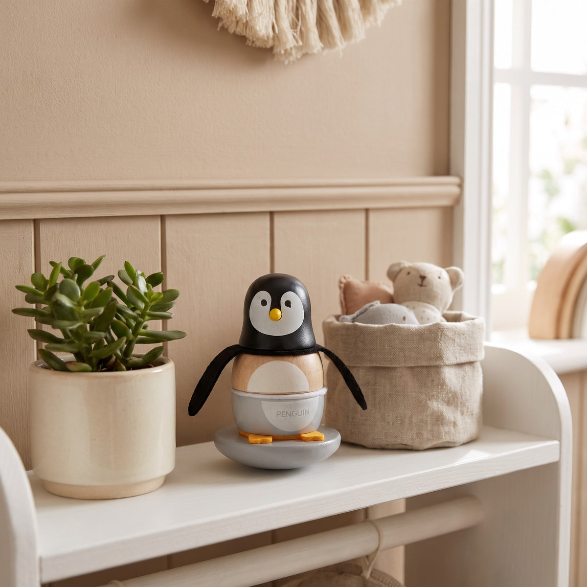 Wooden penguin stacker on a white nursery shelf beside a plant and a linen basket