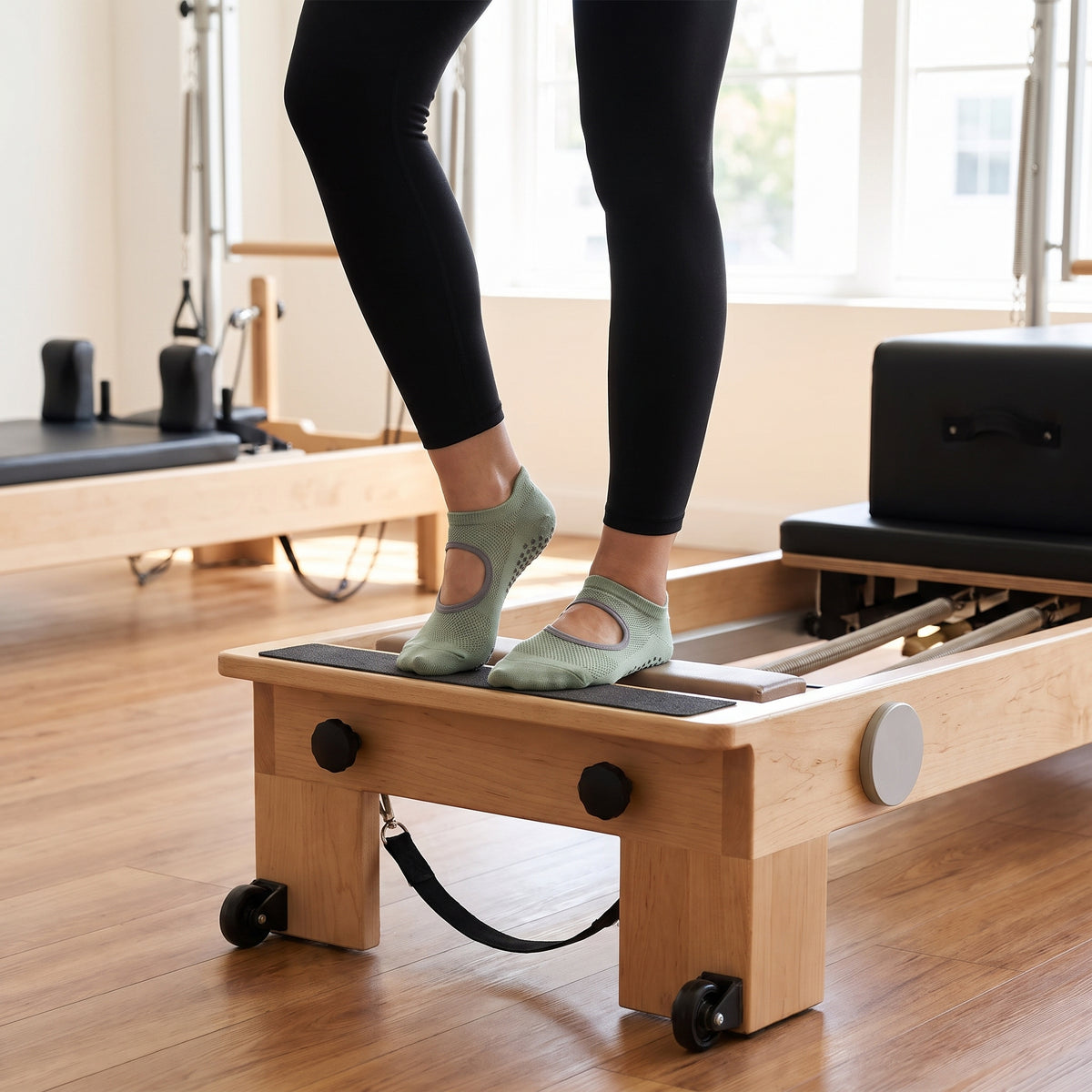 Woman on a pilates reformer wearing sage grip socks