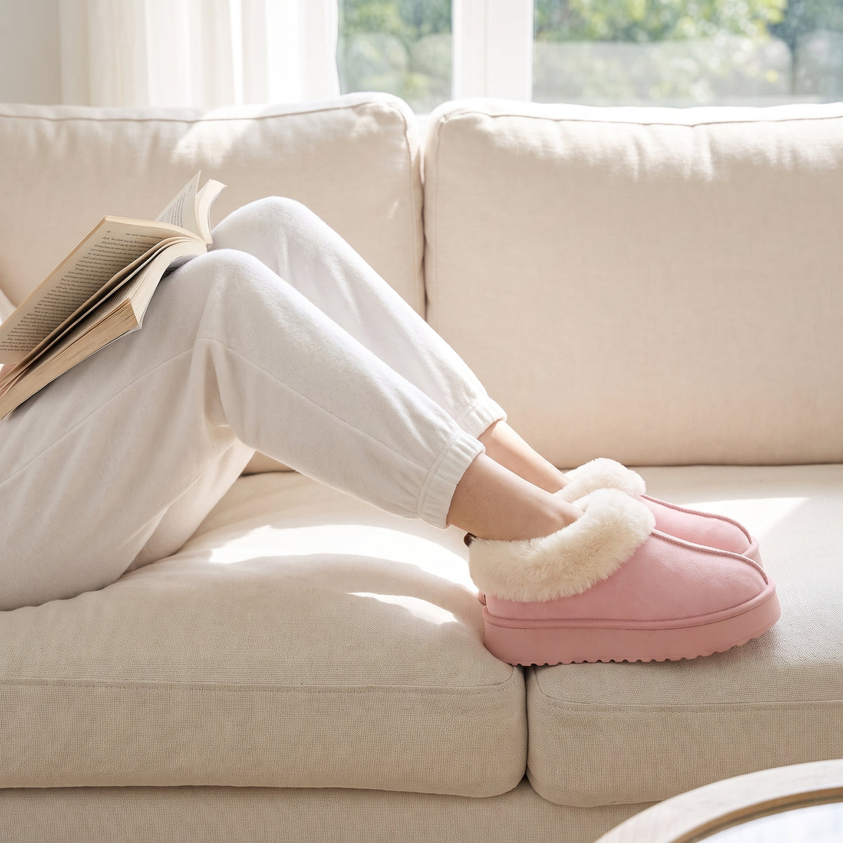 Woman reading on a sofa wearing pink fluffy platform slippers