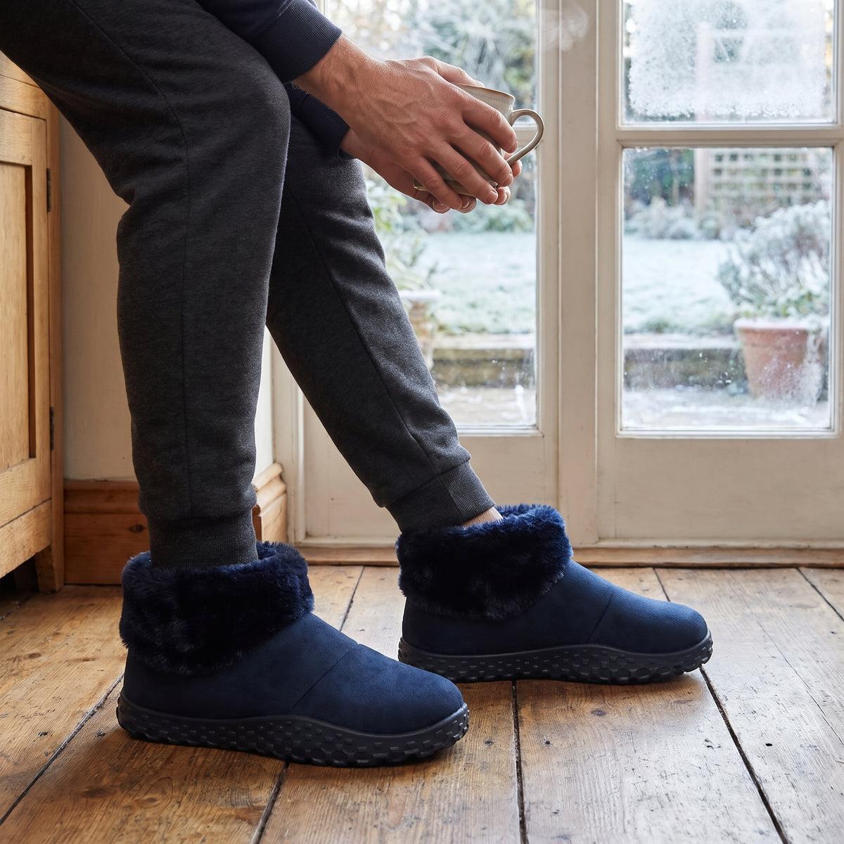 Man in grey joggers wearing navy slipper boots in a kitchen
