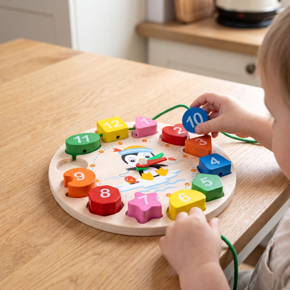 Child threading the blue 10 block onto a green lace beside the wooden clock